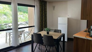 A compact room with a dining table, chairs, a small kitchen area, and a large window with curtains. - 1st floor, swimming pool, hammam, terrace, parking, tv, 27m², Pra Loup (Jausiers)