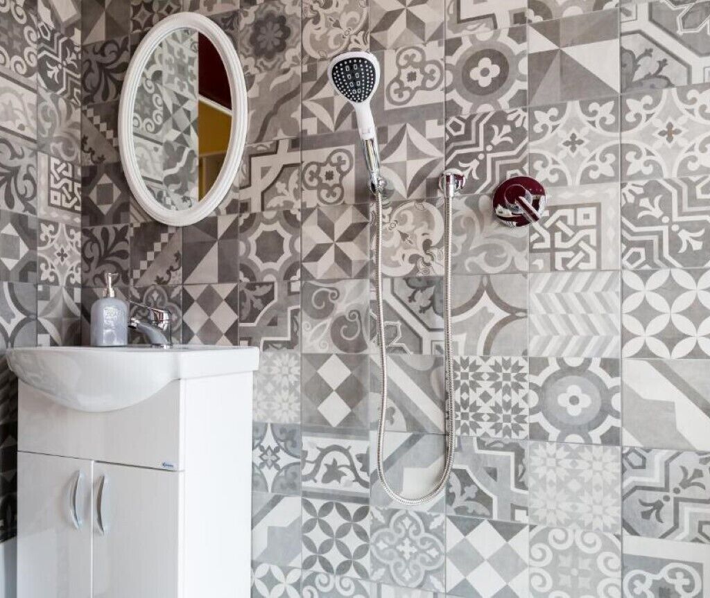 A bathroom with patterned tiles, a white sink, and a shower with a handheld showerhead.