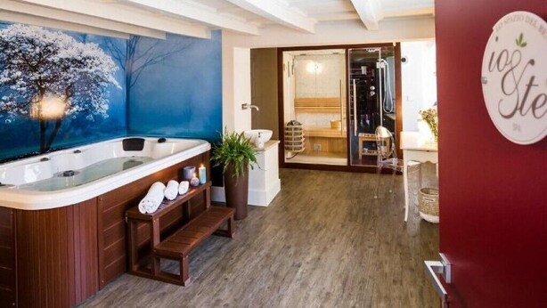 A modern bathroom with a freestanding bathtub, wooden benches, and a large window with a view of trees. - Io&Te wellness space (Sordevolo)