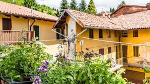 A yellow building with a tiled roof, a balcony, and a garden with purple flowers. - Io&Te wellness space (Sordevolo)