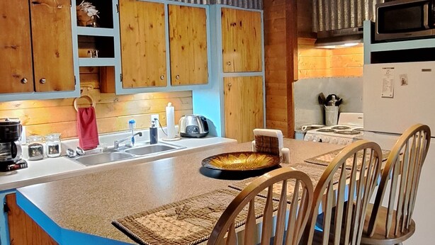 A kitchen with wooden cabinets, a blue countertop, and a central island with chairs. - Holly's Hideaway, Cabin in the Woods (Nogal)