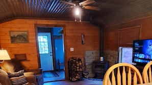 A cozy cabin interior with a wooden ceiling, a sofa, a dining table with chairs, a fireplace, and a television. - Holly's Hideaway, Cabin in the Woods (Nogal)