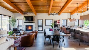 A spacious living area with a fireplace, wooden ceiling beams, a dining table, and a kitchen area with bar seating. - 5 King Beds on Golf Course with a VIEW 0.6 mile walk to Winery! (Cle Elum)