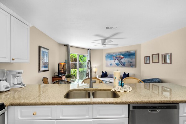A kitchen with a double sink, white cabinets, a coffee maker, and a ceiling fan.