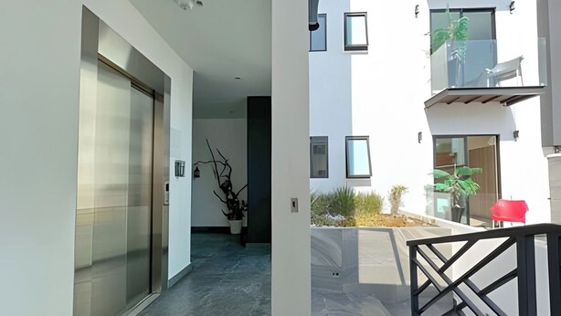 Un bâtiment moderne avec une entrée dotée d’une porte en verre, un balcon avec une chaise rouge et un petit jardin.