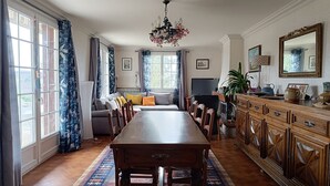 Ruokailutila, jossa on puinen pöytä ja tuolit, kattokruunu ja sohva.