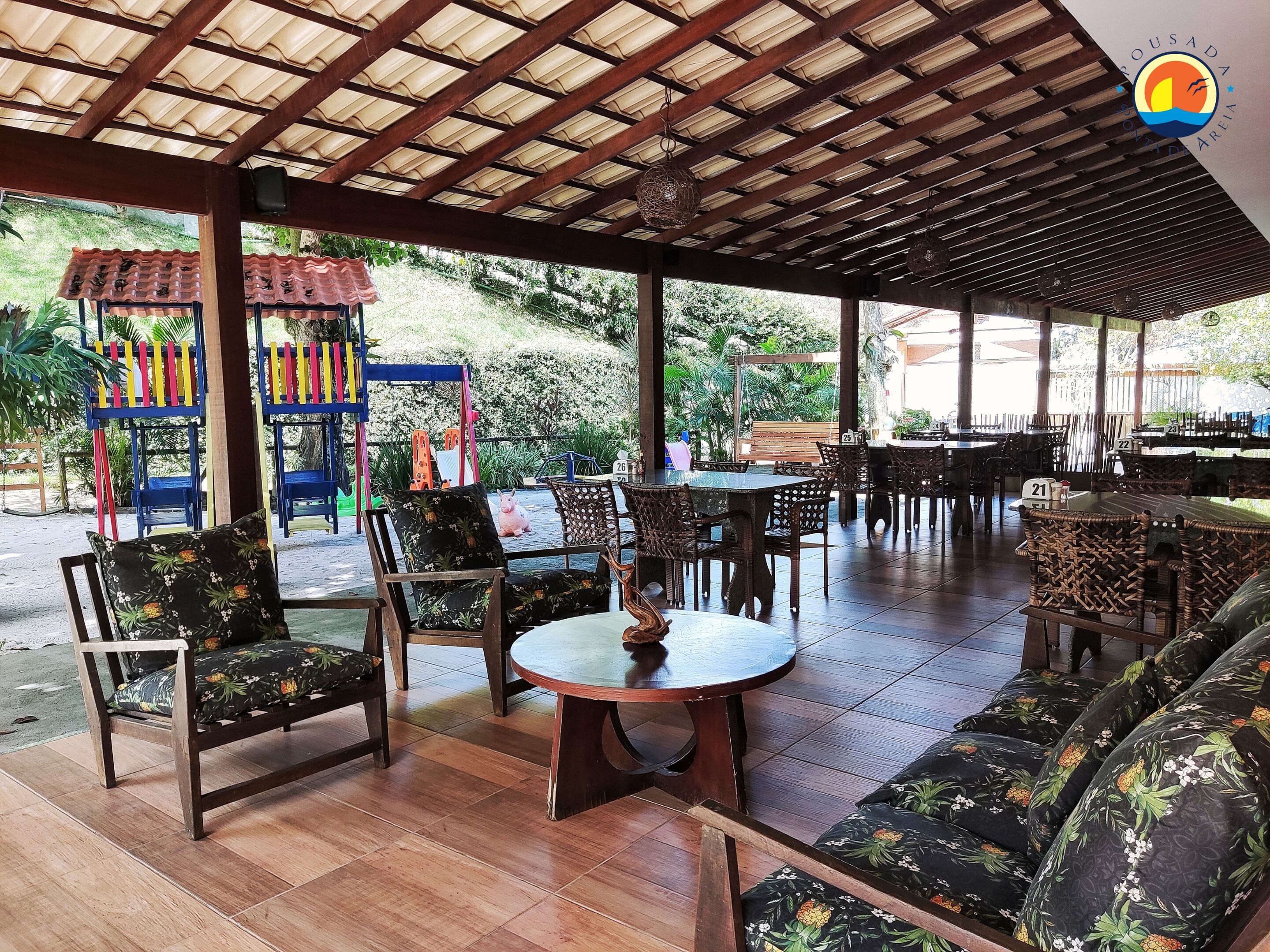 An outdoor seating area with wooden tables and chairs, a play structure, and a covered patio.