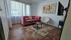 A living room with a pink sofa, a white chair, a coffee table, and a painting on the wall. - COMPLEJO RAICES PATAGONICAS DUPLEX CALLE LOS PRUNUS (Dina Huapi)