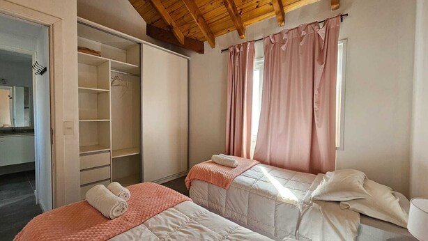 A bedroom with two beds, a wardrobe, and a window with curtains. - COMPLEJO RAICES PATAGONICAS DUPLEX CALLE LOS PRUNUS (Dina Huapi)