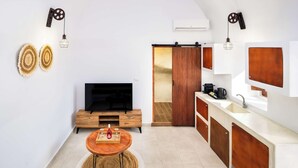 A modern kitchen with a TV, wooden cabinets, and a dining area with a round table. - Santorini Luxury Suite w/ Rooftop HotTub & SeaView (Akrotiri, Santorini)