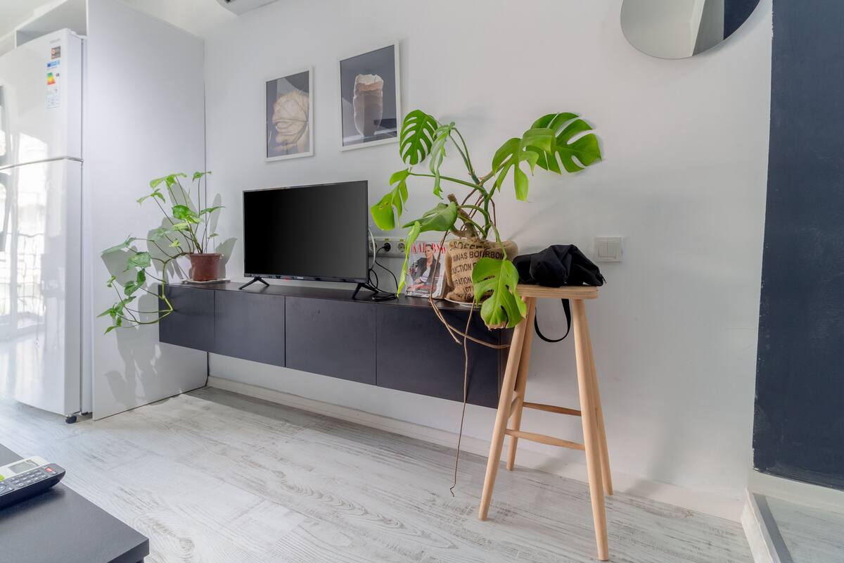 Una cocina moderna con un refrigerador empotrado, un televisor de pantalla plana y un taburete de madera con una planta en maceta.