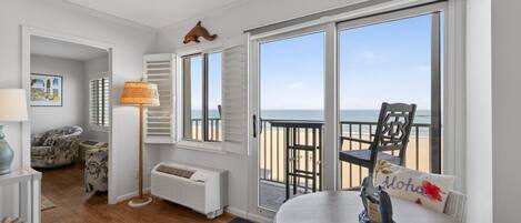 Een kamer met uitzicht op het strand, een ronde tafel met een decoratief kussen, een lamp en een stoel.
