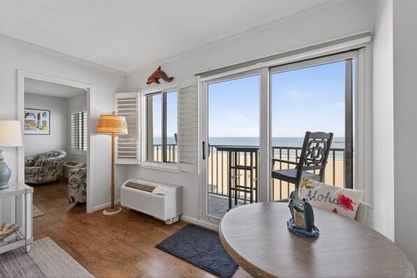 A room with a view of the beach, a round table with a decorative pillow, a lamp, and a chair.