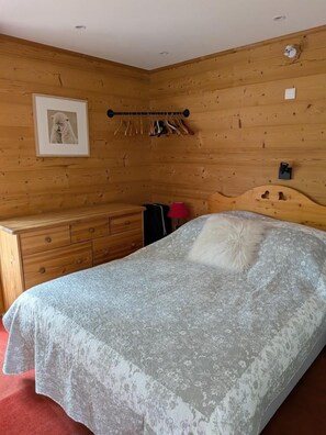 Een slaapkamer met een houten hoofdbord, een bed met een beddegoed met een patroon, een dressoir en een kapstok met hangers.