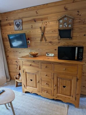 A wooden cabinet with drawers, a television mounted on the wall, and a microwave on top of the cabinet.