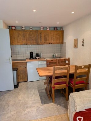 A compact kitchen with wooden cabinets, a white dishwasher, and a dining table with chairs.