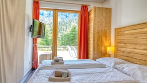 Camera d'albergo con due letti, una TV e vista sugli alberi dalla finestra.