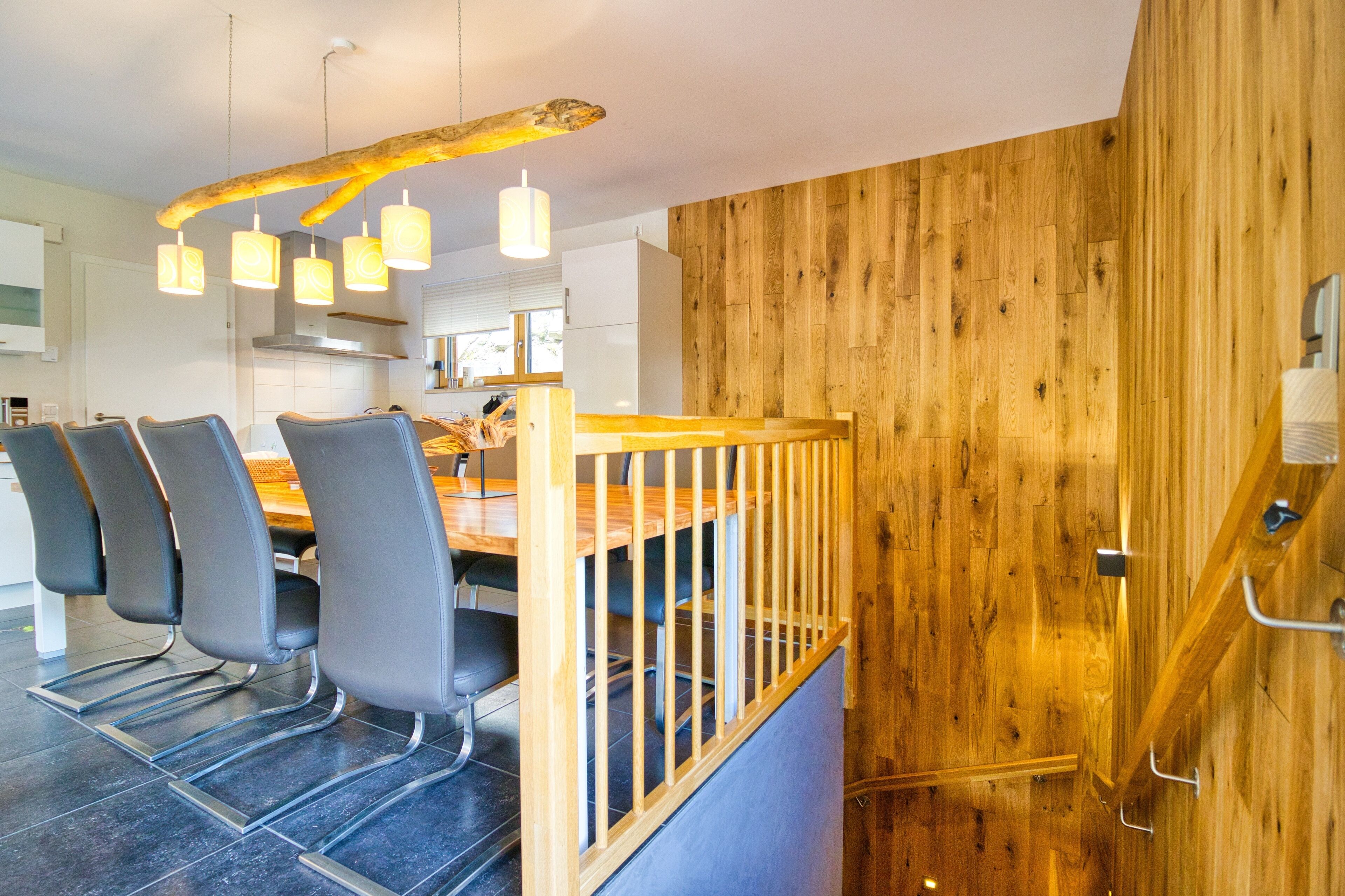 A modern kitchen with a wooden accent wall, a dining area with chairs, and a unique ceiling light fixture.
