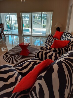 Un salon moderne avec un grand canapé à motifs zébrés, des coussins rouges et une table basse en verre.
