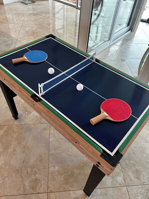 Ein Tischtennistisch mit zwei Schlägern und zwei Bällen auf einem Fliesenboden.