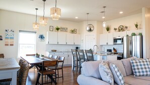A modern kitchen with white cabinets, stainless steel appliances, and a dining area with a wooden table and chairs. - Beautiful Beachfront Home with Beach Access. (Sargent)