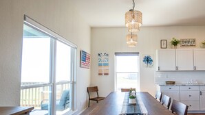 A spacious dining area with a long wooden table, several chairs, and a hanging light fixture. - Beautiful Beachfront Home with Beach Access. (Sargent)