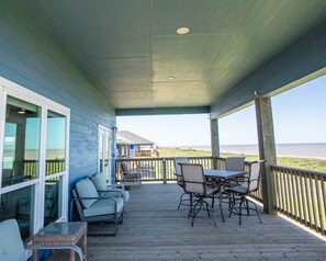 A covered outdoor deck with seating and a view of the ocean. - Beautiful Beachfront Home with Beach Access. (Sargent)