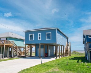 A two-story house with a balcony, wooden stairs, and a view of the ocean. - Beautiful Beachfront Home with Beach Access. (Sargent)