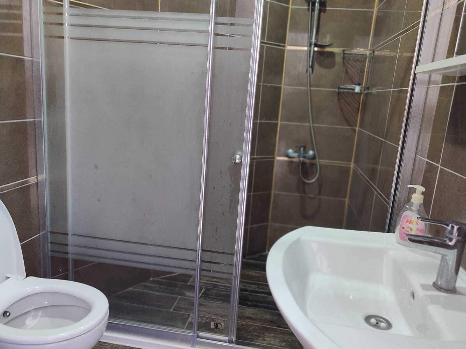 Casa de banho com chuveiro em cabine de vidro, lavatório branco e sanita.