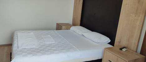 A neatly made bed with a checkered blanket and pillows, a wooden nightstand with drawers, and a dark headboard.