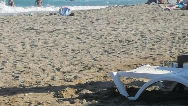 Una playa con gente nadando y relajándose. Hay sillas de playa y sombrillas en la arena.