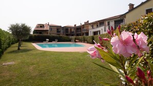 A swimming pool surrounded by a well-maintained lawn and a row of residential buildings in the background. - Regarda - Miralago 2, bike apartment with pool, lake view, garage (Lazise)