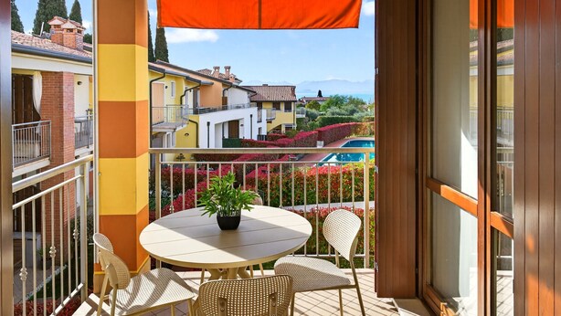 A balcony with a round table and chairs, a potted plant, and a view of buildings and mountains. - Regarda - Miralago 2, bike apartment with pool, lake view, garage (Lazise)