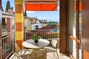 Un balcon avec une table ronde et des chaises, un pot de fleurs et une vue sur des immeubles et des montagnes.