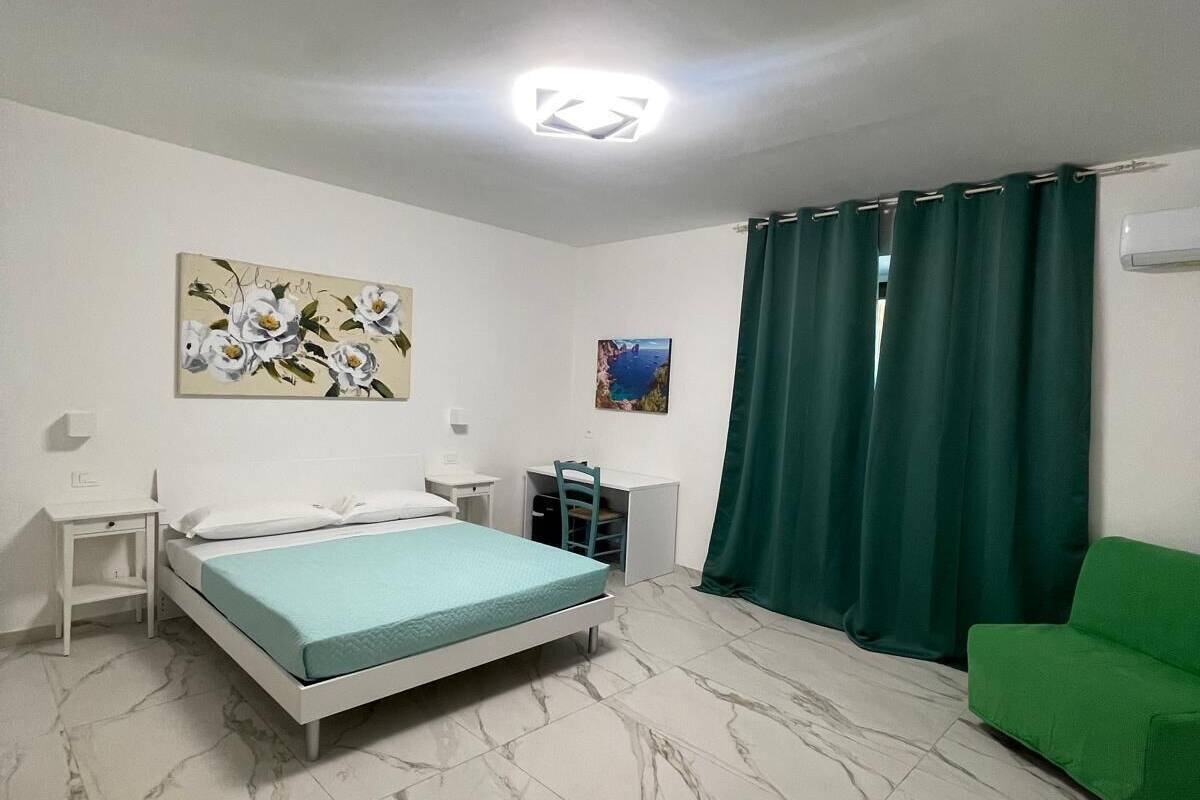 Un dormitorio con una cama, un escritorio, una silla, un sofá verde y un cuadro en la pared.
