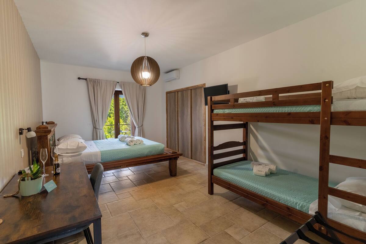 Una habitación con dos camas, una mesa de madera con una planta, una lámpara colgante y una ventana con cortinas.