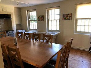 A spacious kitchen with a large wooden table and chairs, a built-in oven, and a window with a view of trees. - Stunning Hall Cottage, near York and Leeds (Wighill)