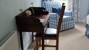 Habitació amb escriptori de fusta, una cadira, un radiador, una finestra amb cortines i un sofà blau i blanc a escacs.