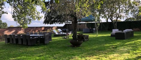 A grassy outdoor area with a dining table and chairs, a barbecue grill, and lounge chairs.