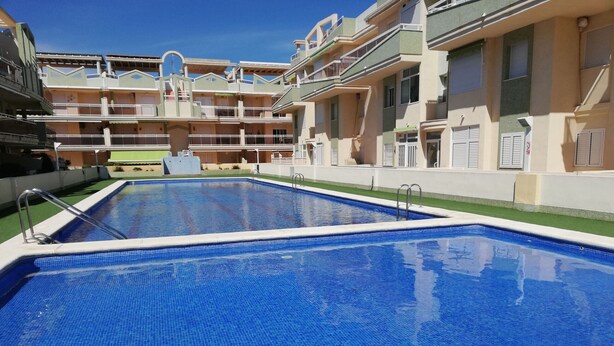 Une piscine avec une terrasse carrelée et un bâtiment doté de balcons en arrière-plan.