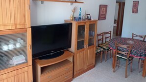 Un salon équipé d’un téléviseur à écran plat, de meubles en bois, d’une table à manger avec des chaises et d’une étagère ornée d’objets décoratifs.