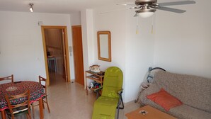 Un salon comprenant une table à manger, des chaises, un canapé, un fauteuil vert, une table basse en bois et un ventilateur de plafond.