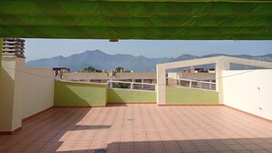 Une terrasse sur le toit, agrémentée d’un auvent végétal, d’un sol carrelé et offrant une vue sur les montagnes lointaines.