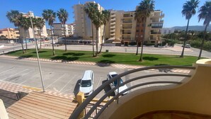 Blick vom Balkon auf einen Parkplatz mit einem weißen Auto, Palmen und mehrstöckigen Gebäuden im Hintergrund.