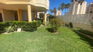 Ein gepflegter Innenhof mit einem ordentlich gestutzten Rasen, einer kleinen Gartenanlage mit Sträuchern und einem Baum sowie einem weißen Zaun.
