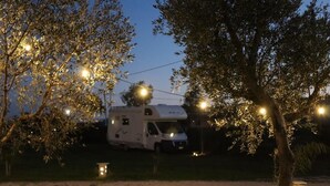 A white RV parked in a grassy area with string lights and a small lantern. - Campeggio in Fattoria (Serre)