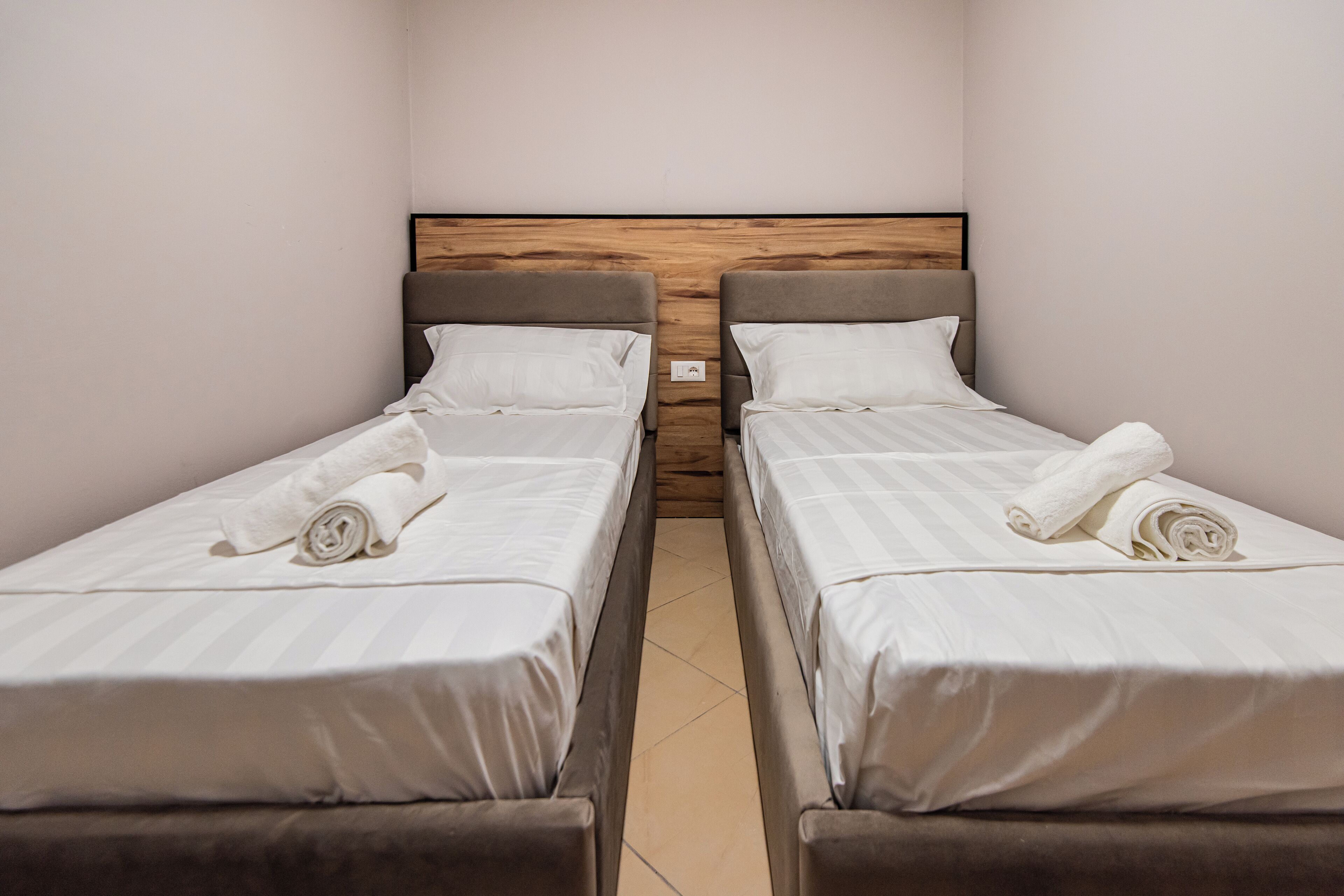 A hotel room with two single beds, each with a wooden headboard and white linens.