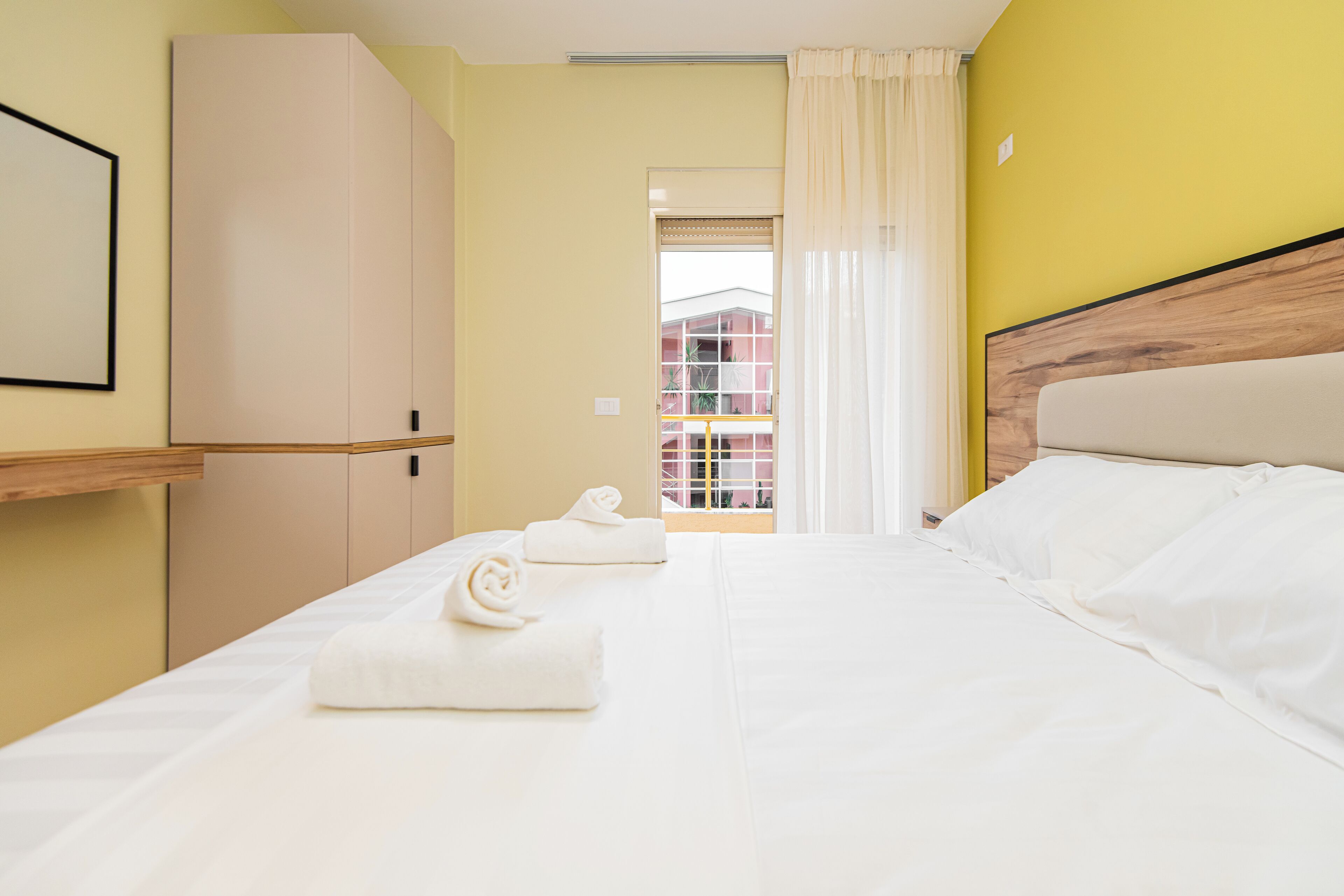A hotel room with a bed, a wardrobe, and a view of a building through a window.