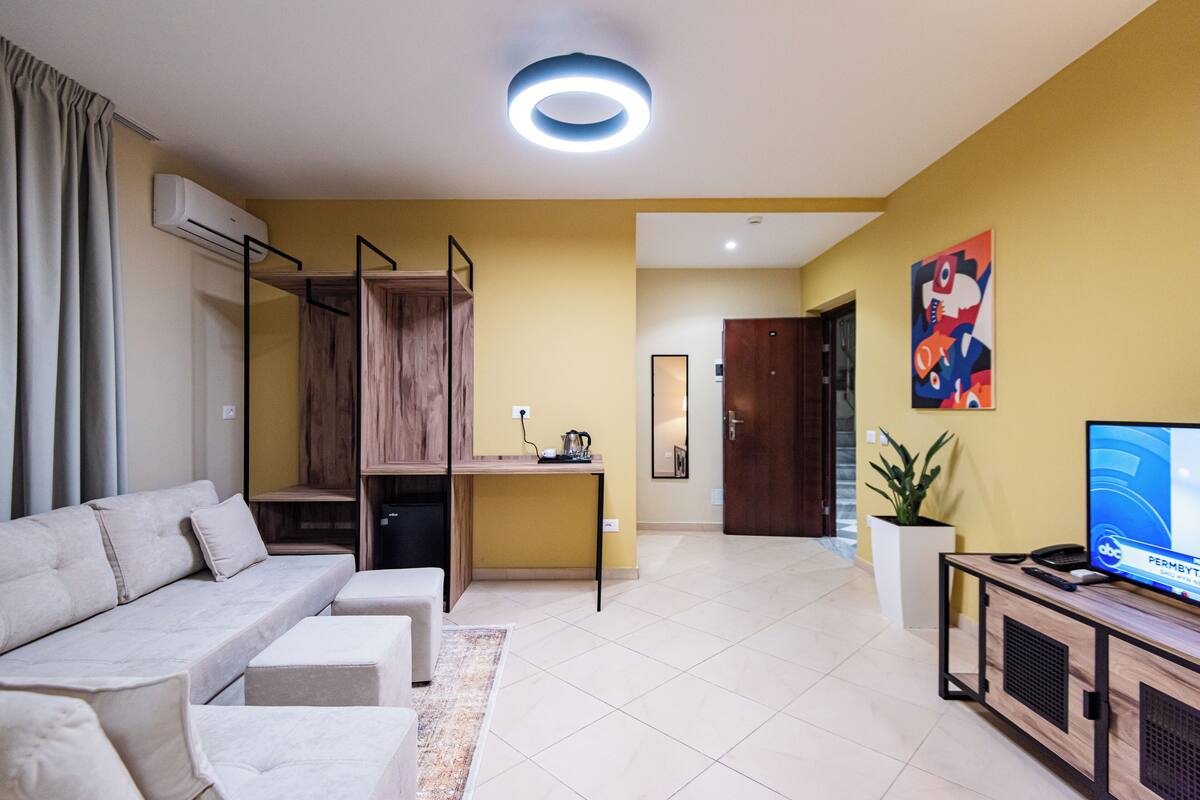 A modern living room with a sofa, a small table, a TV, and a staircase leading to another room.