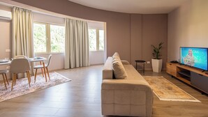 Una sala moderna con sofá, televisor, comedor y ventanas amplias.